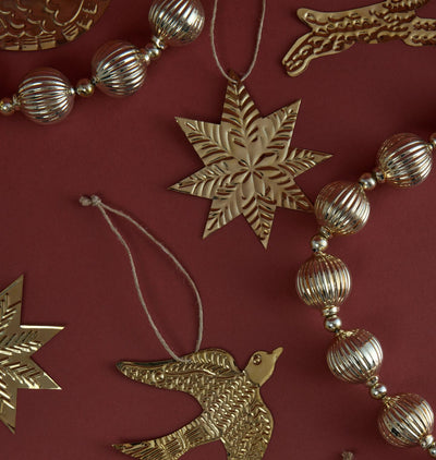 A styled flat-lay of metallic Christmas ornaments on a dark burgundy background, featuring a central gold star and silver bead garlands.