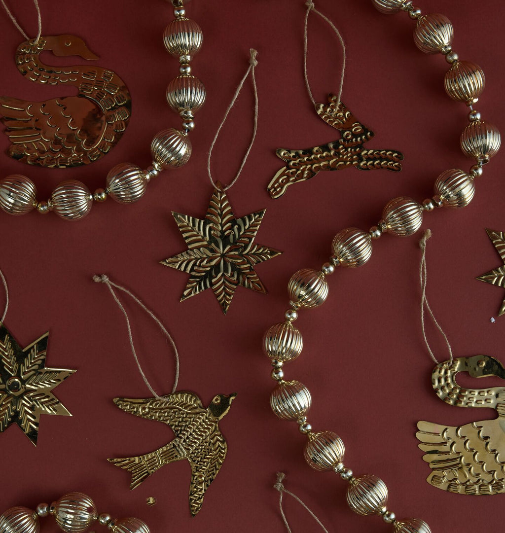 A close-up of a holiday garland featuring metallic gold bird and star ornaments interspersed with ribbed gold beads, laid out on a dark red background.