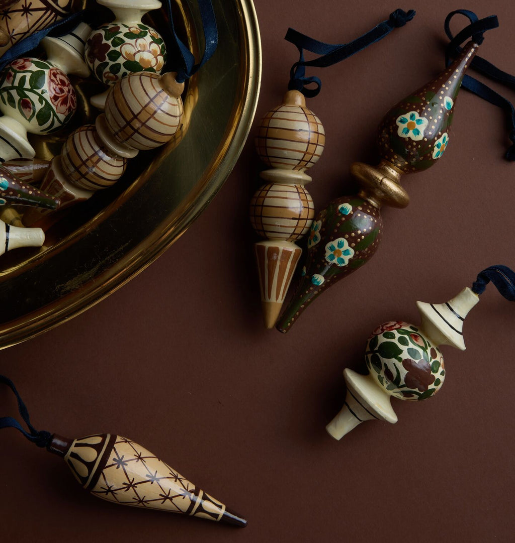 Hand-painted wooden Christmas ornaments with intricate patterns, displayed on a dark brown background with a gold tray partially visible.