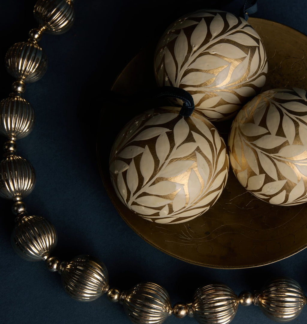 A group of hand-painted wooden ornaments, decorated with a gold leaf pattern on a rich blue background, arranged in a vintage brass bowl.