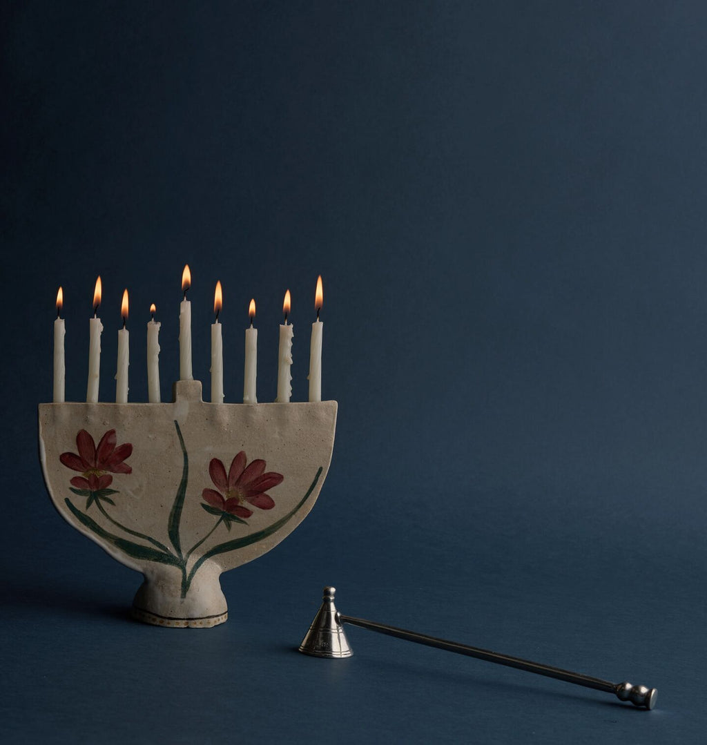 A hand painted ceramic menorah with lit candles against a rich blue background 