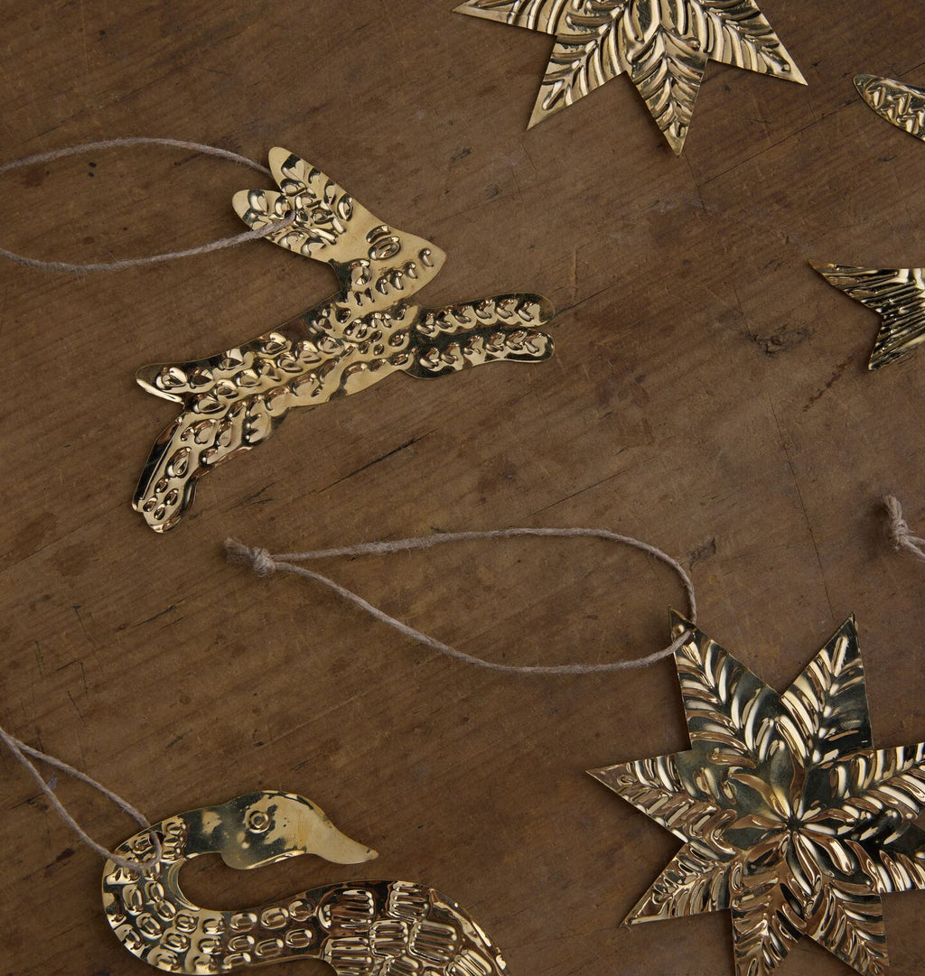 A styled flat-lay of metallic Christmas ornaments on a wood background, featuring a central gold rabbit and stars
