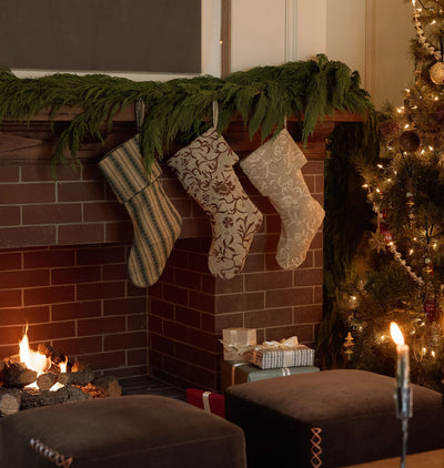 A warm christmas scene with a lit brick fireplace and three embroidered stockings hung on the mantle 