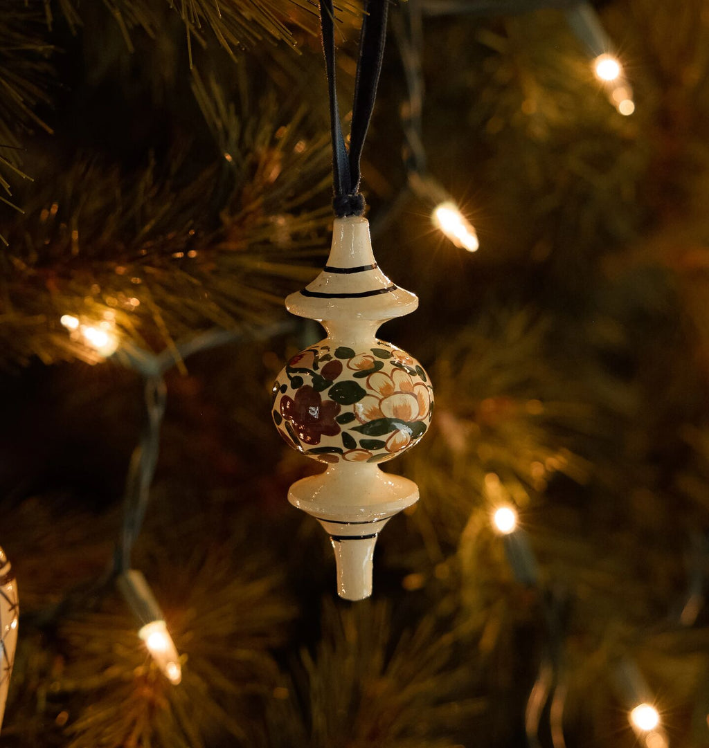 A hand-painted wooden Christmas ornament with intricate patterns, shown on a lit christmas tree