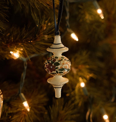 A hand-painted wooden Christmas ornament with intricate patterns, shown on a lit christmas tree