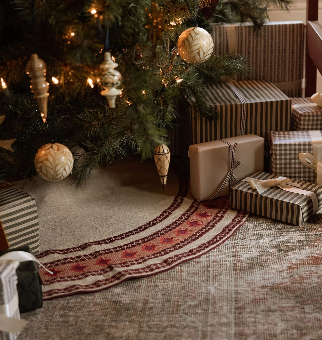 A christmas scene of an embroidered tree skirt under a styled tree with wrapped gifts 