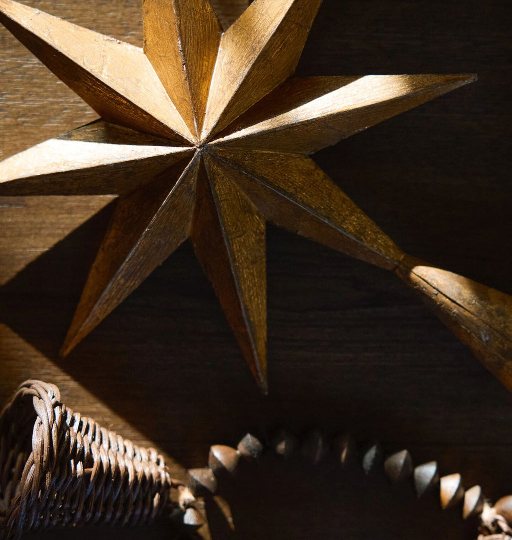 A close up of a golden painted metal rustic star tree topper on a wooden background