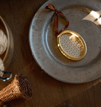 A golden oval picture frame with a rust colored velvet ribbon tie show laid out on a vintage plate