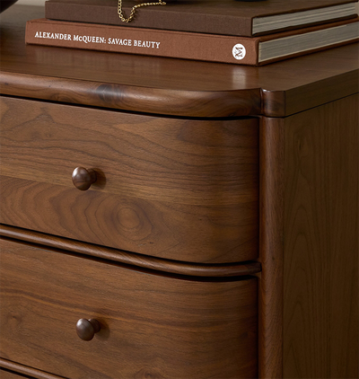 A close up corner shot of a five-drawer wooden chest of drawers with a curved front and small round knobs