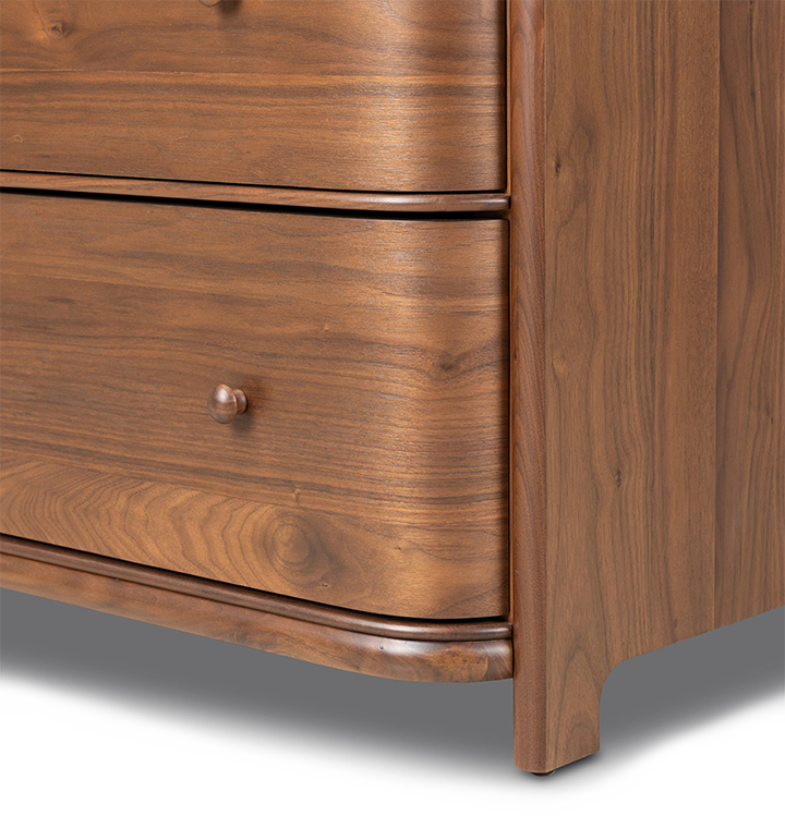 A close up corner shot of the bottom of a five-drawer wooden chest of drawers with a curved front and small round knobs