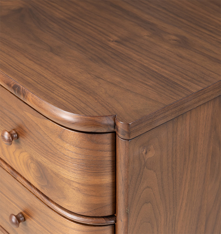 A close up corner shot of a five-drawer wooden chest of drawers with a curved front and small round knobs