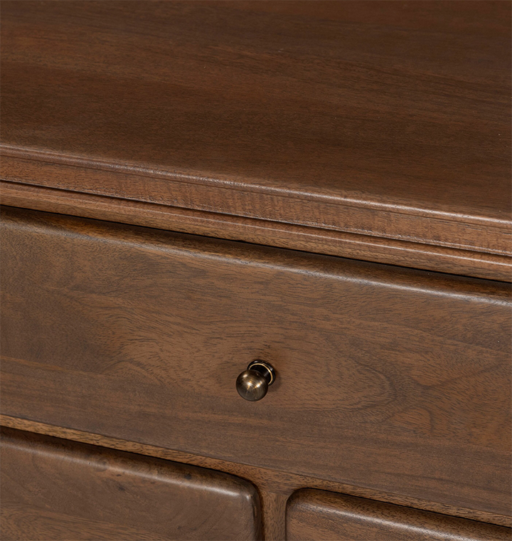A close up view of a wooden dresser with small round brass knobs, shown against a plain light gray background.