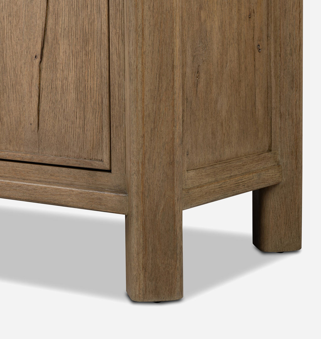 Close-up of a rustic medium-brown wooden cabinet corner showing the wood grain texture, panel details, and sturdy block legs on a light gray background.