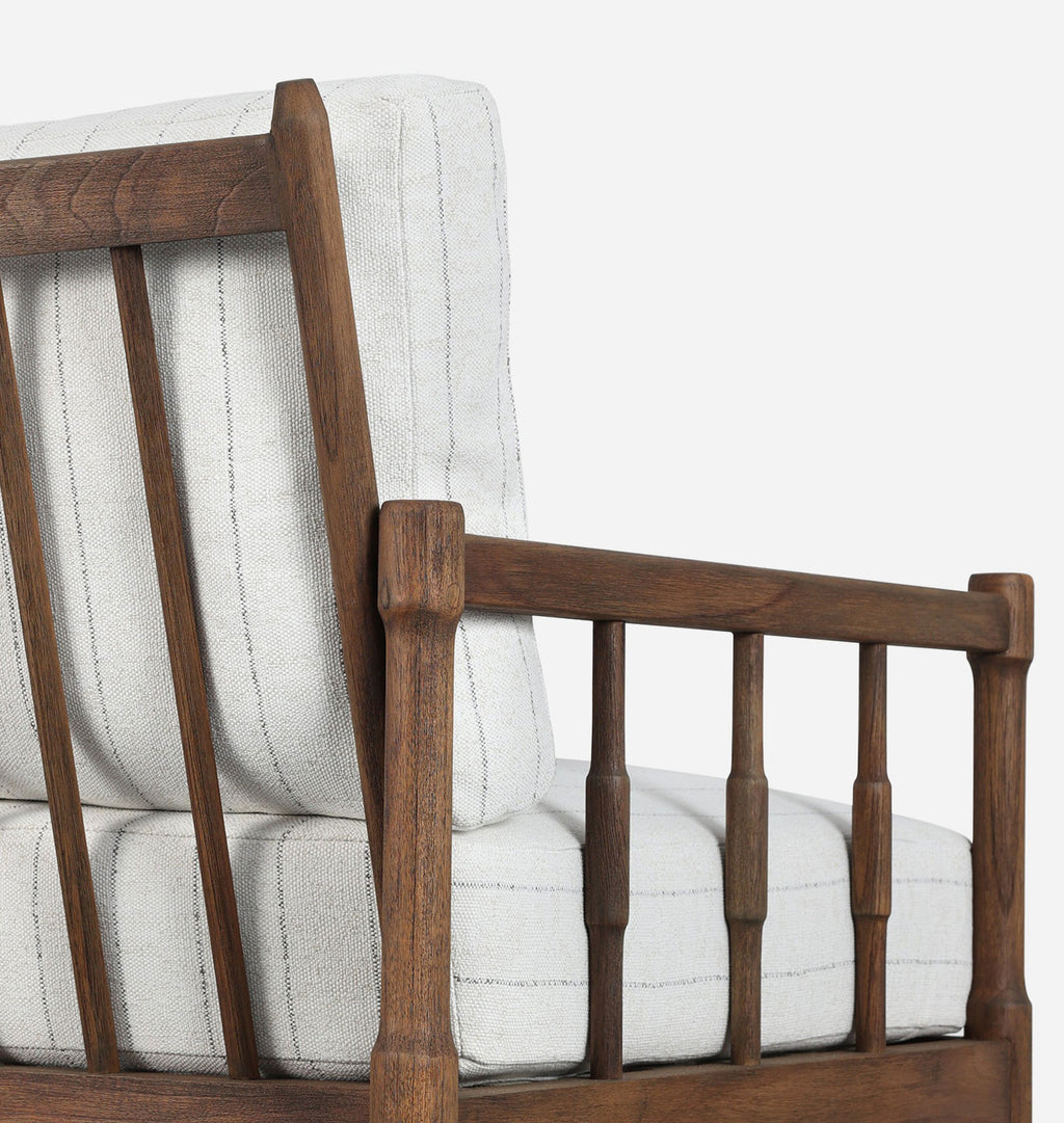 Close-up of a wooden outdoor armchair with thick off-white upholstered cushions and a spindle-back design, shown against a plain light gray background.