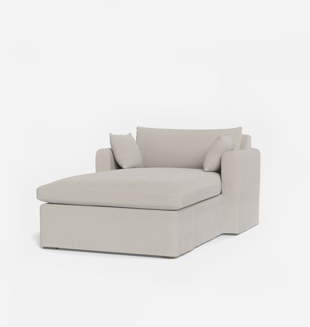 A light beige upholstered chaise lounge chair with two matching back cushions, shown on a clean white background.