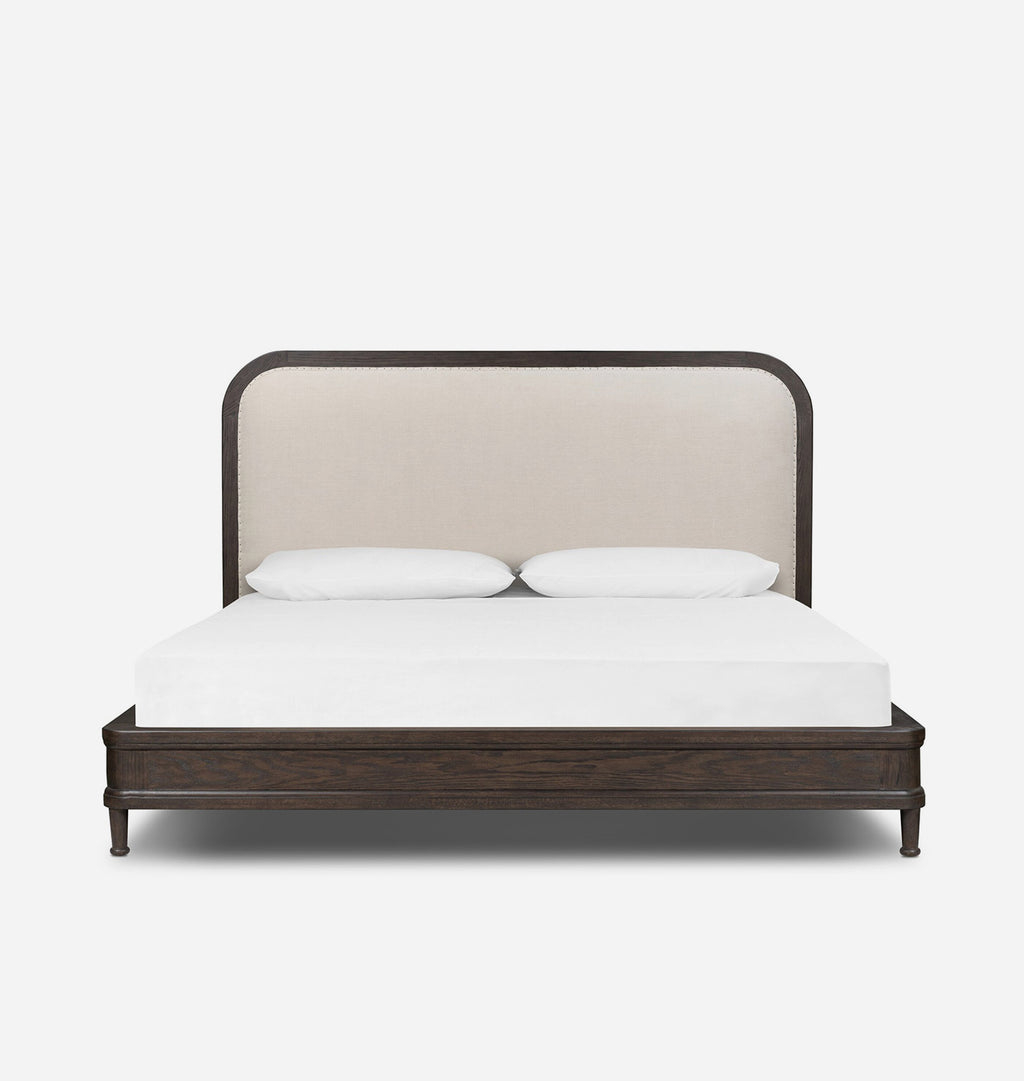 A modern platform bed with a dark wood frame and a tall, curved upholstered headboard in a light beige fabric, shown with a white mattress and two white pillows against a plain white background.