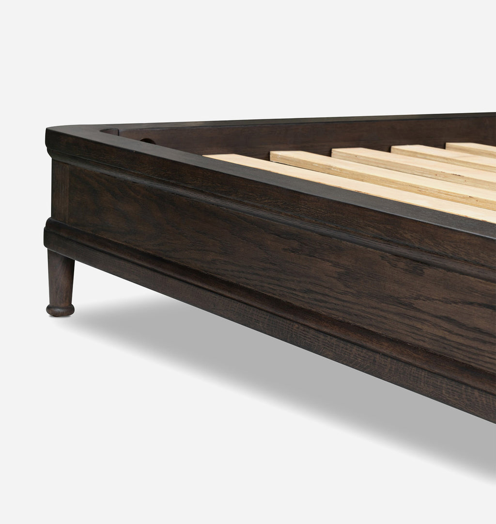 Close-up of a dark brown wooden bed frame corner with a turned leg and light natural wood slats, shown on a clean light gray background.