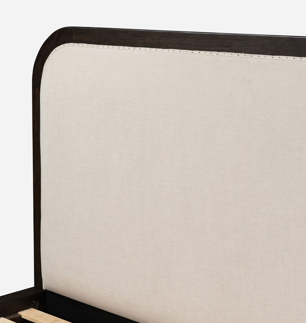 Close-up of a bed headboard with a dark wood frame and a large off-white upholstered panel, shown against a plain light background.