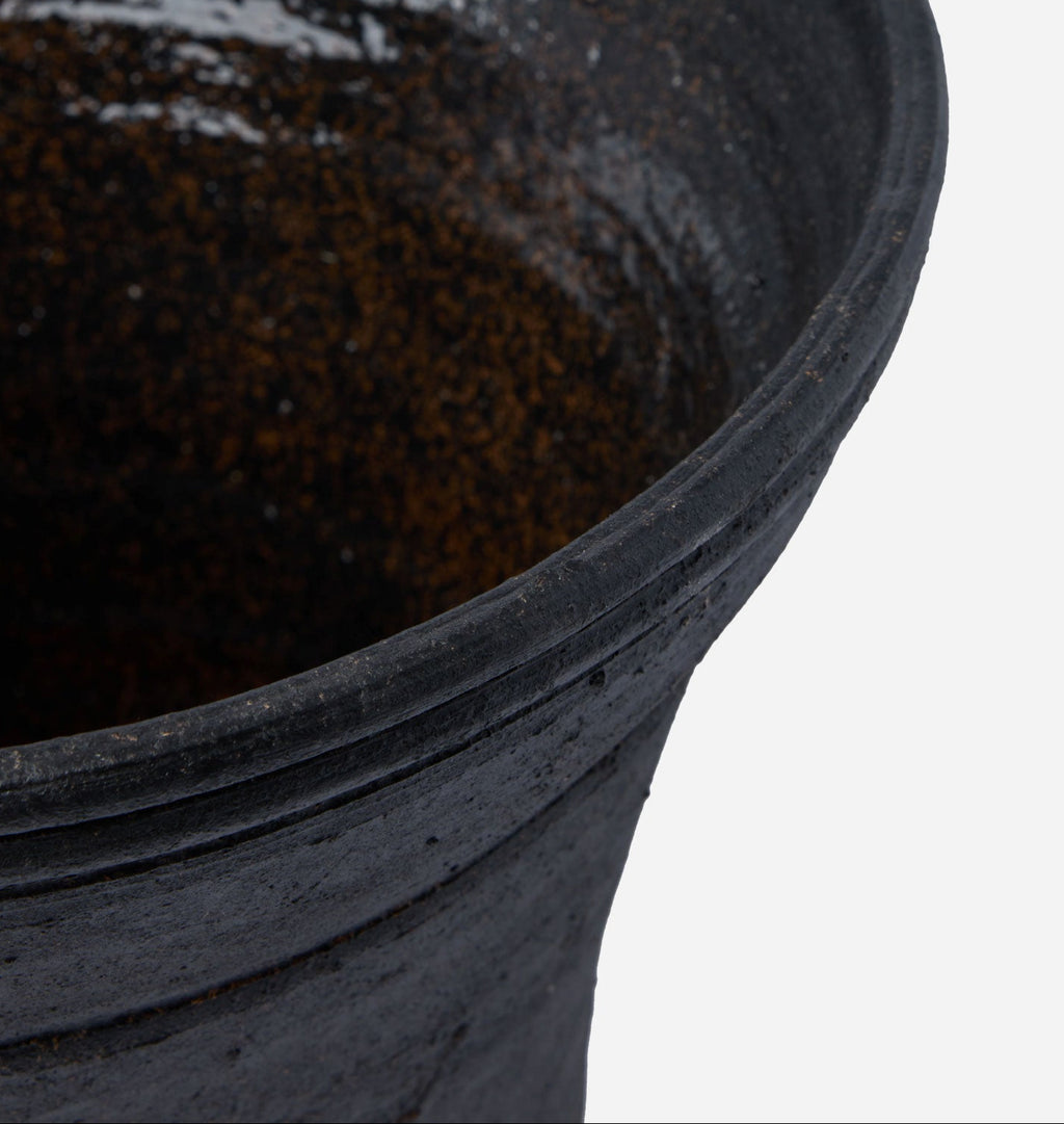 Close-up detail of a dark textured ceramic pot rim with a glossy black finish, set against a plain white background.