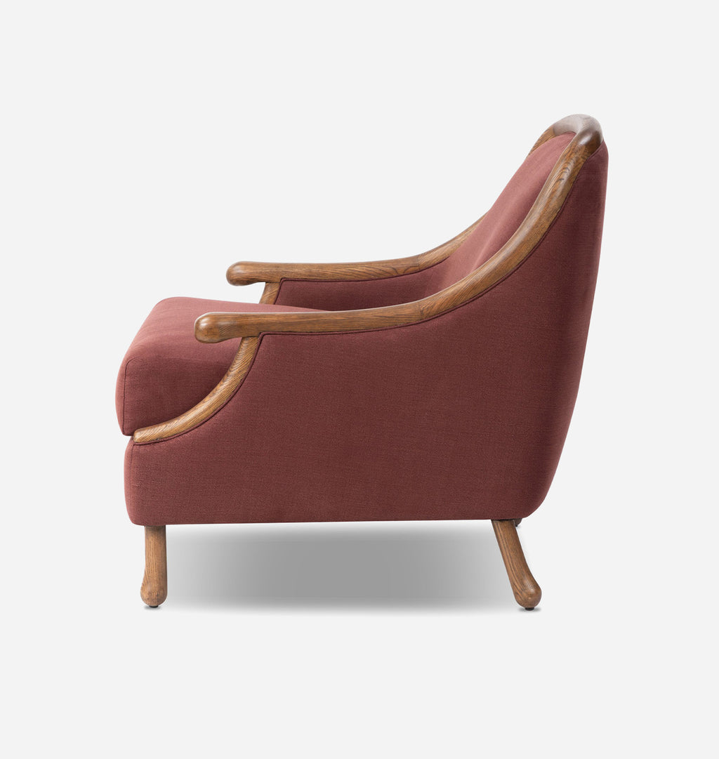 A classic accent chair upholstered in a dusty terracotta red fabric with natural wood arms and legs, shown from a side profile view against a light gray background.