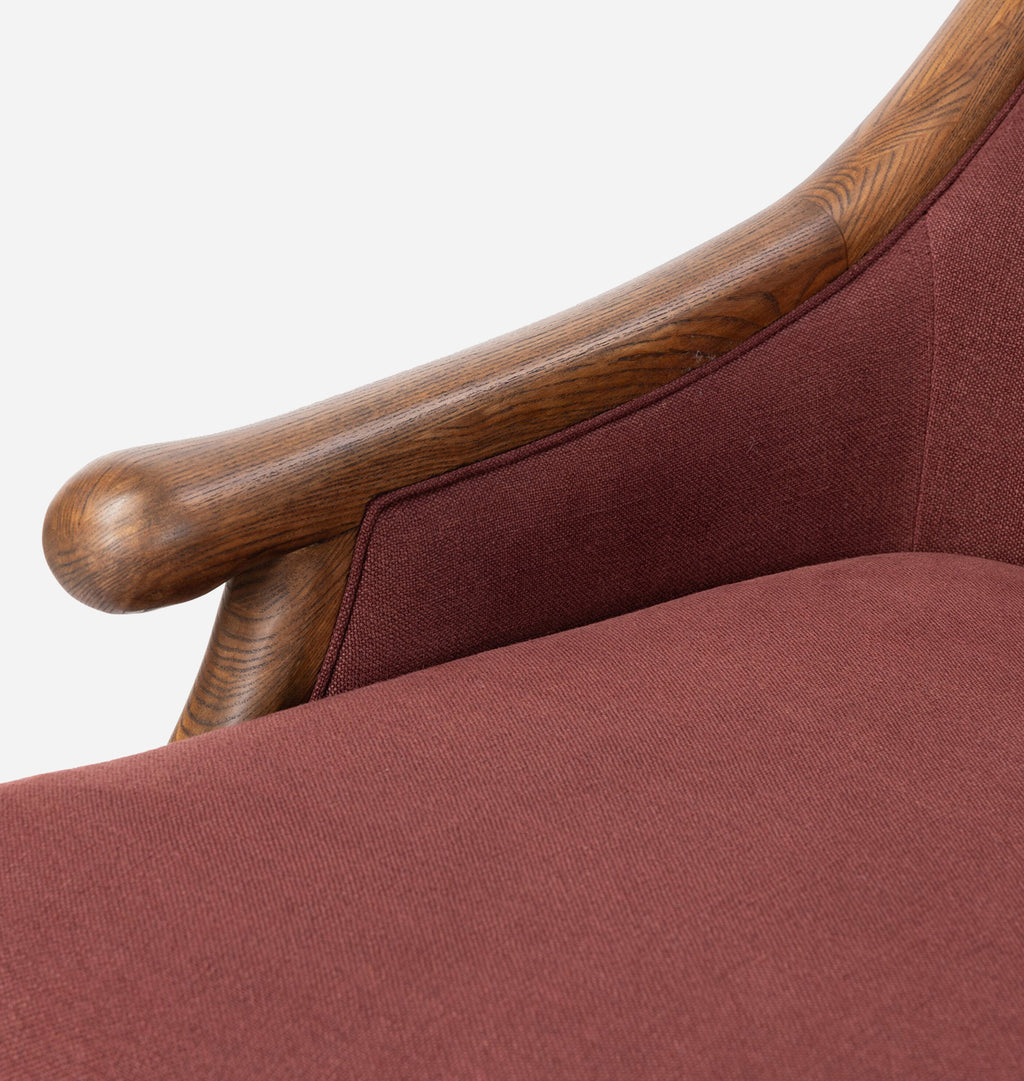 Close-up detail of a mid-century modern armchair featuring a curved medium-brown wooden armrest and textured rust-red fabric upholstery.