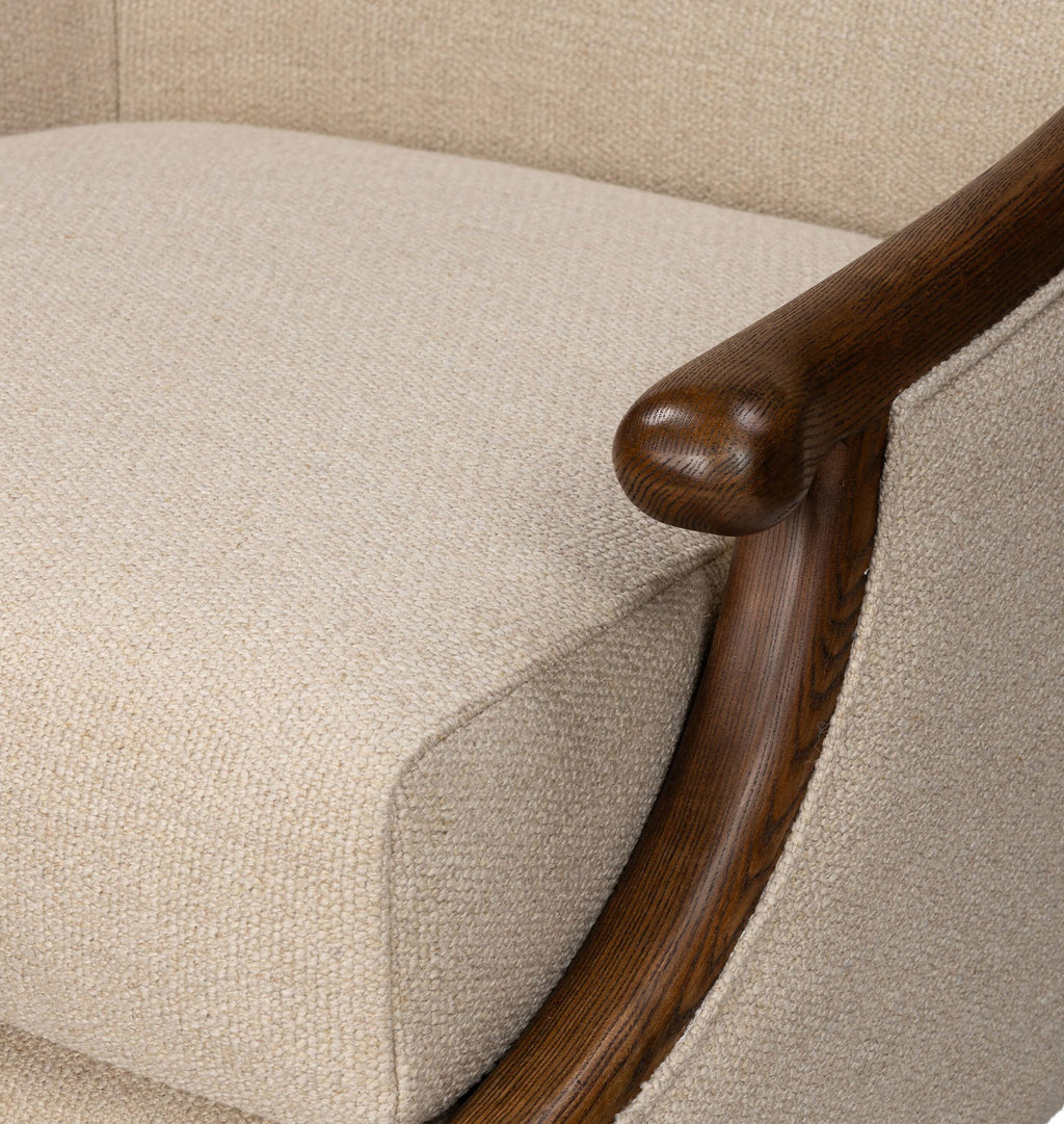 Close-up of a beige textured fabric armchair cushion with a curved dark brown wooden armrest.