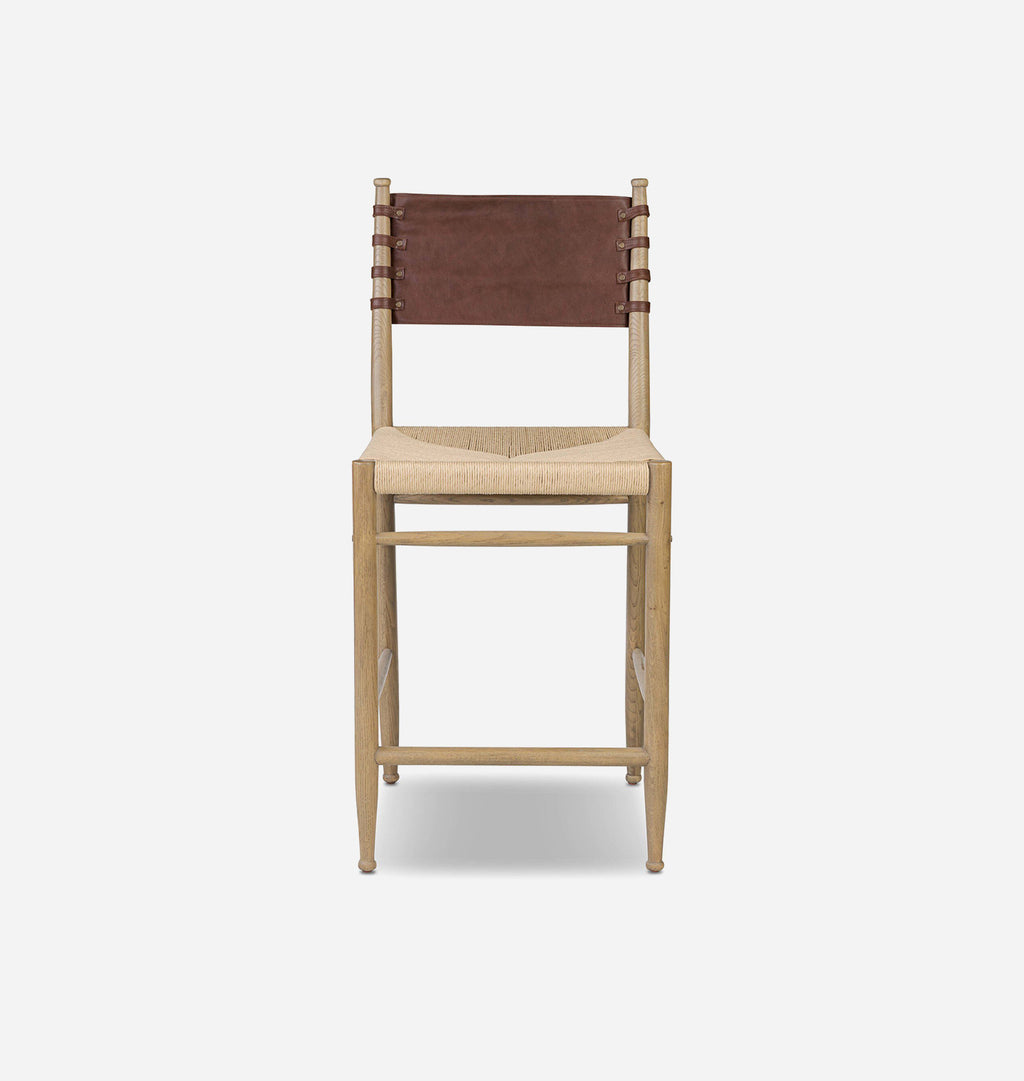 A mid-century modern bar stool with a light natural wood frame, a woven beige rope seat, and a brown leather sling backrest, shown against a plain light gray background.