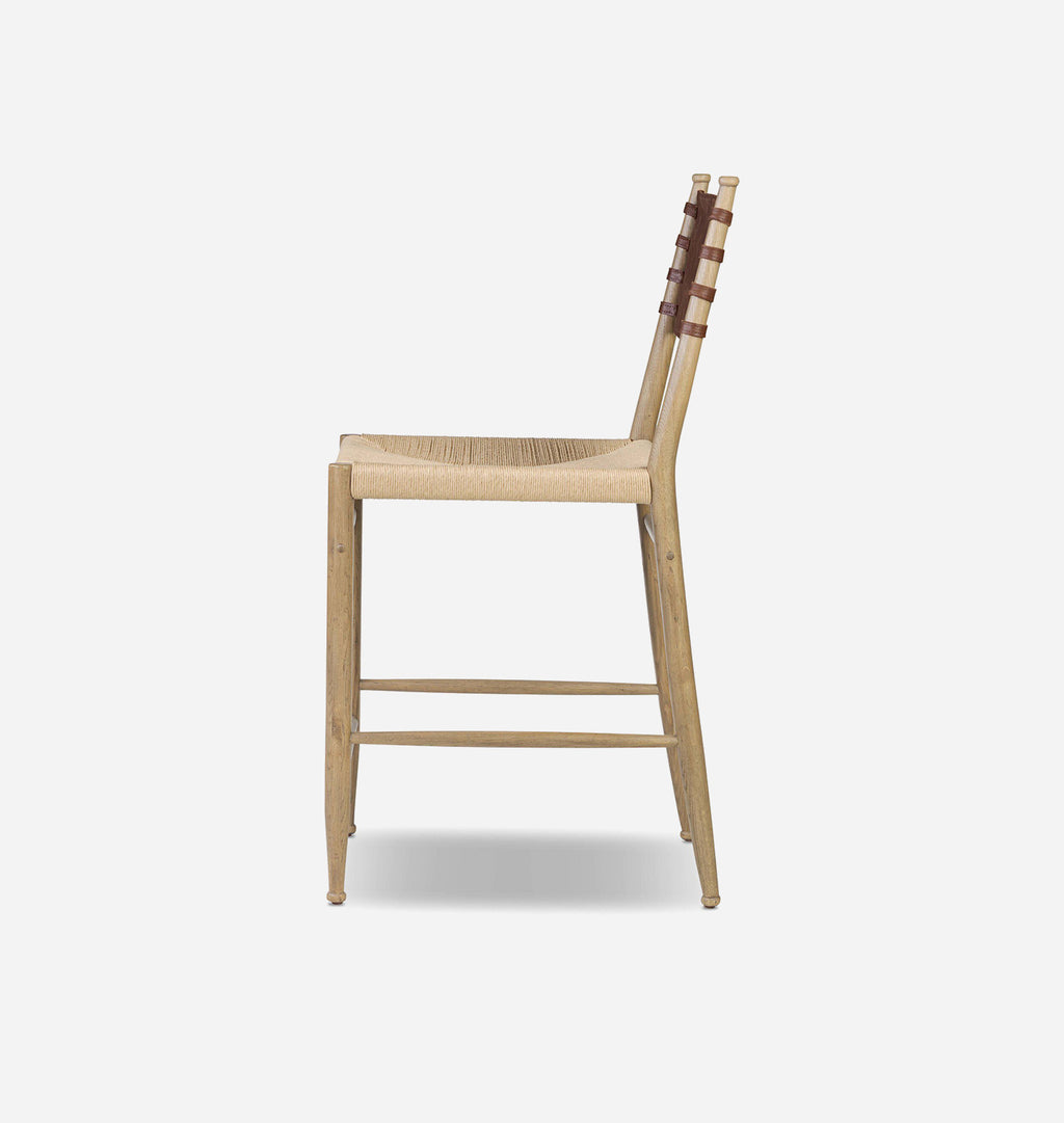 A light natural wood barstool with a woven rope seat and dark brown leather straps on the backrest, shown from a side profile against a light gray background.