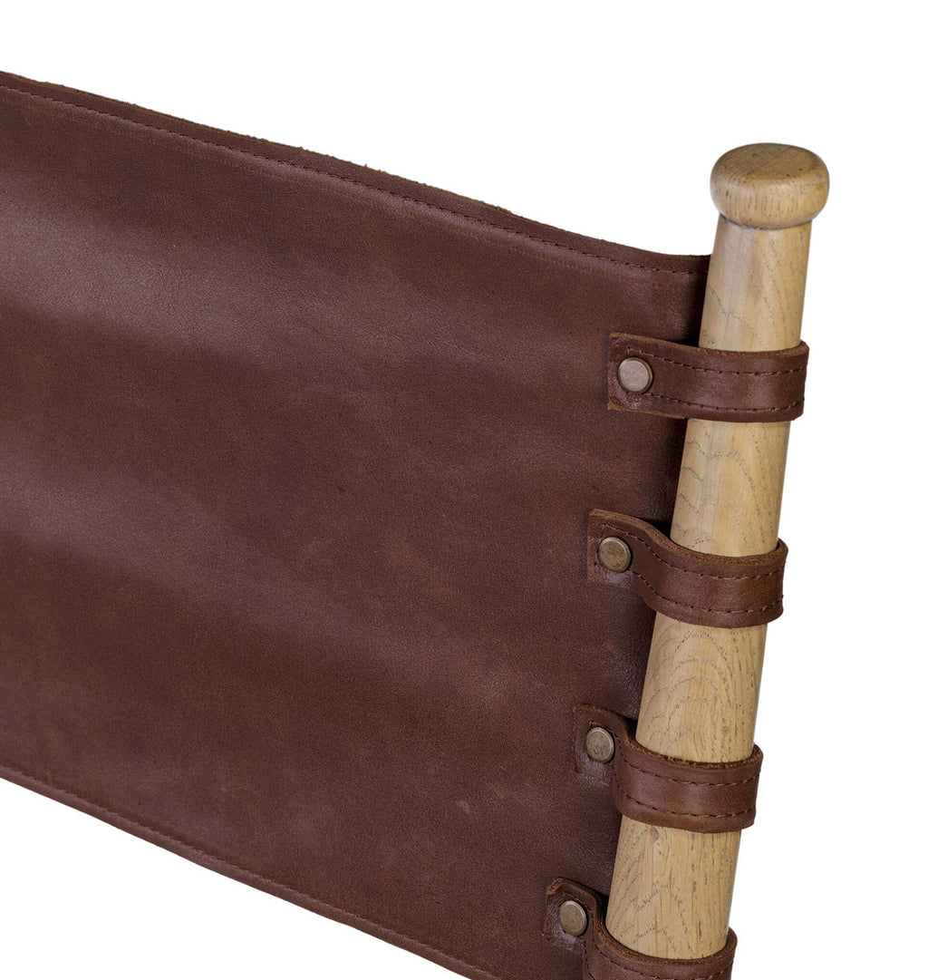 Close-up of a brown leather sling seat or hammock strap attached to a light natural wood pole with metal rivets and leather loops, shown on a plain white background.