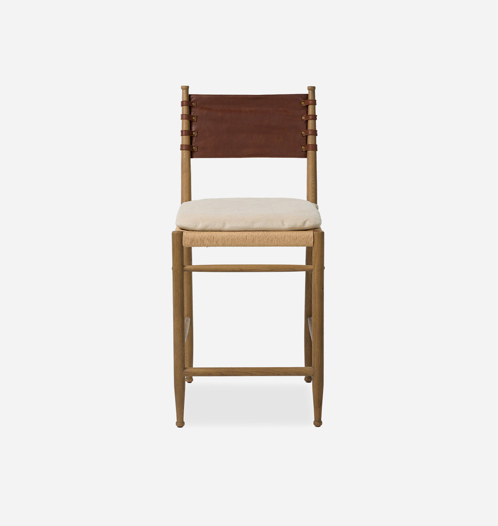A wooden barstool with a natural wood frame, a brown leather sling backrest, and a cream upholstered seat cushion, shown against a plain light gray background.