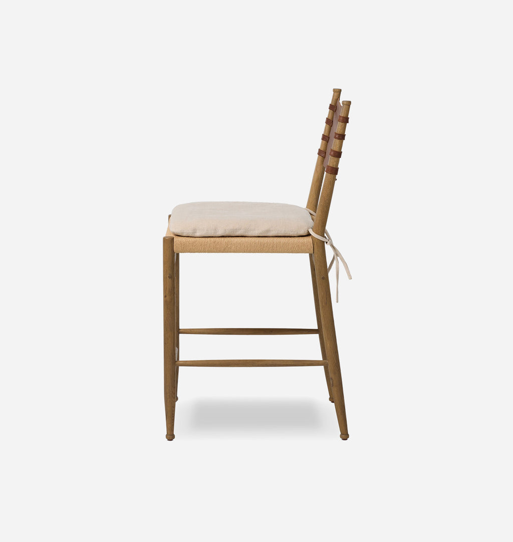 A wooden barstool with a light beige woven seat, a matching tie-on cushion, and a tall ladder-style backrest with brown leather accents, shown from a side profile against a light gray background.