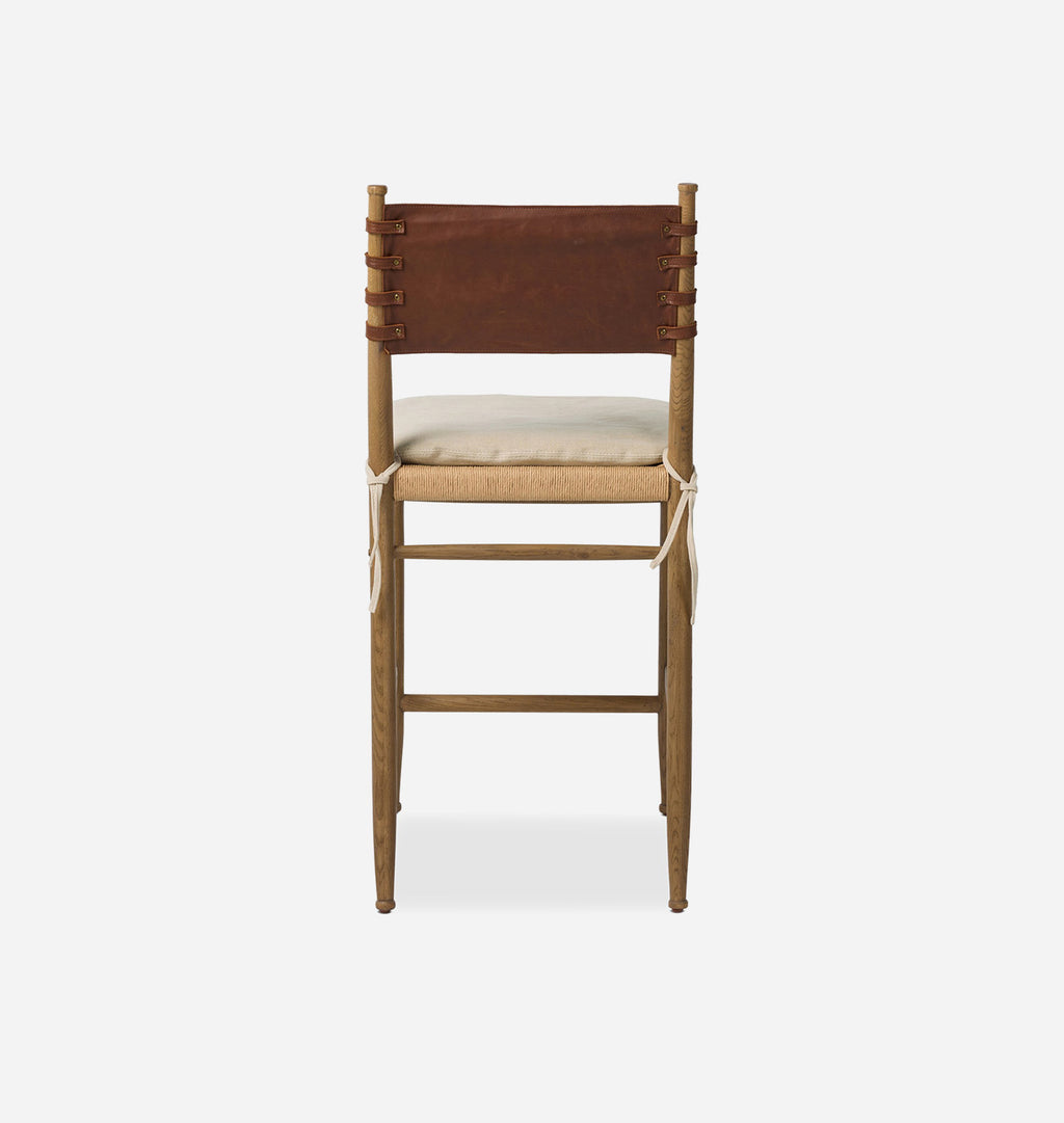 A wooden bar stool with a brown leather backrest, a light beige woven seat, and a cream cushion, shown from the front on a light gray background.