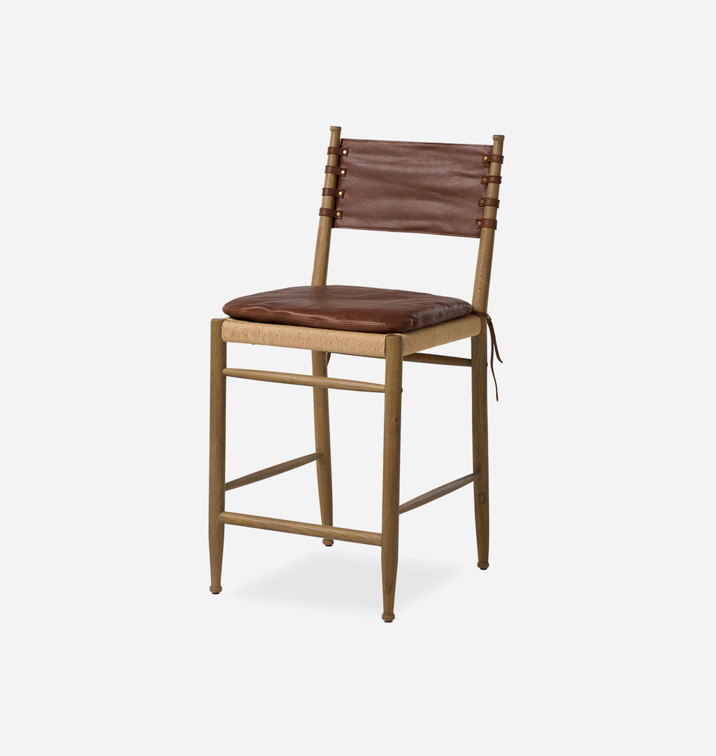 A rustic wooden counter stool with a brown leather seat cushion and backrest, shown from a three-quarter angle against a light gray background.