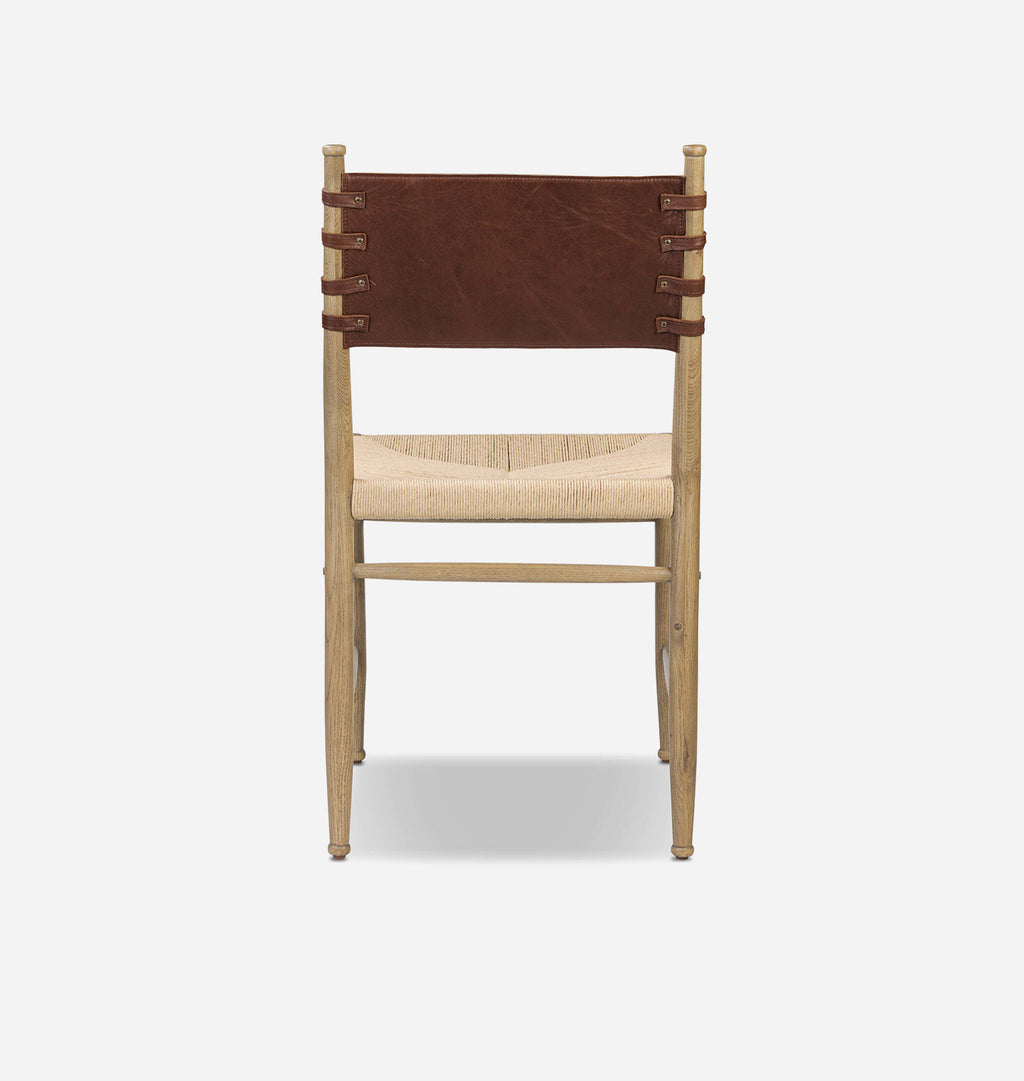A modern wooden dining chair with a natural light wood frame, a woven beige seat, and a dark brown leather sling backrest with leather straps, shown against a light gray background.