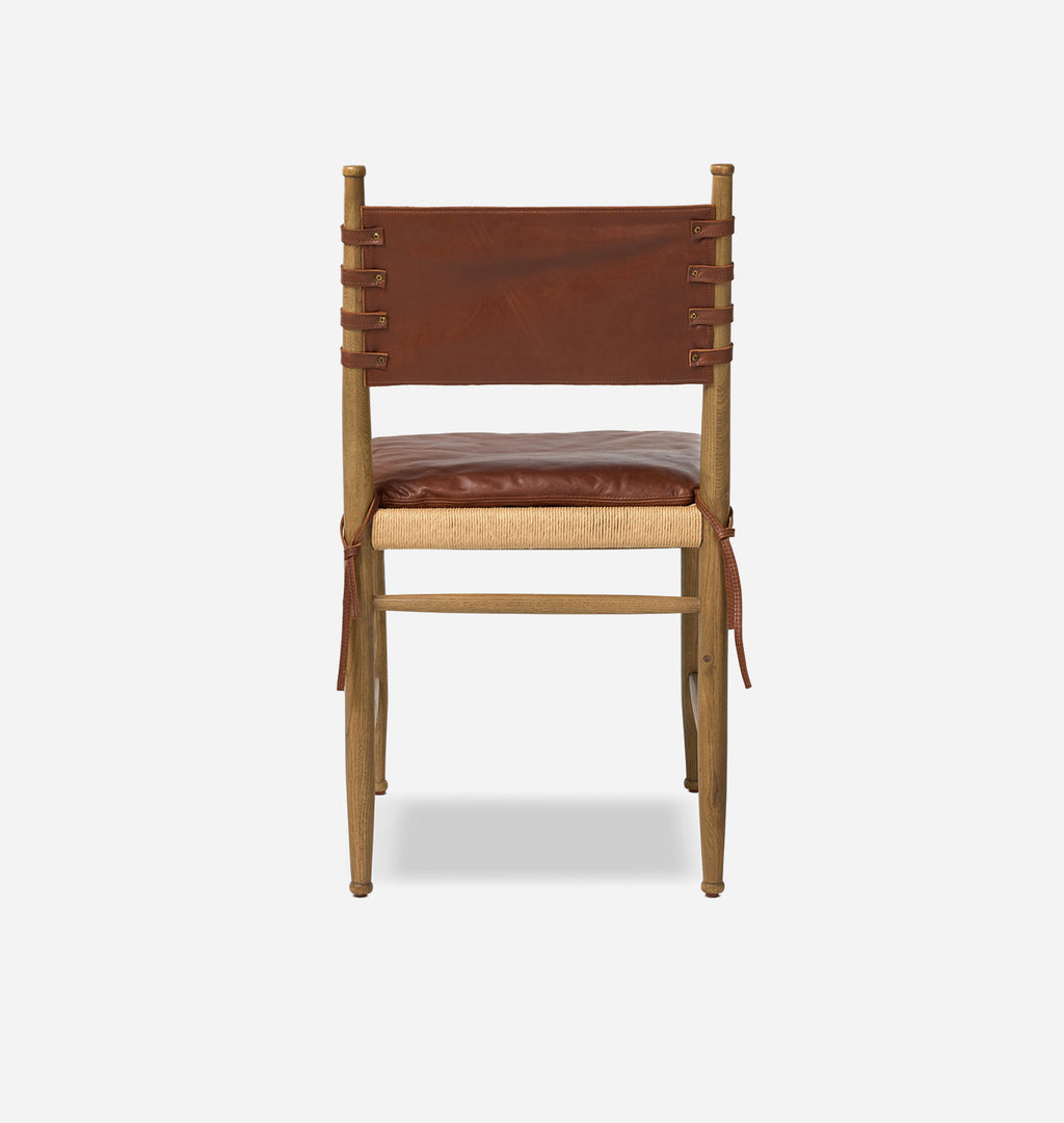 A wooden dining chair with a brown leather seat cushion, a woven natural fiber seat strip, and a brown leather backrest strap, shown against a light gray background.