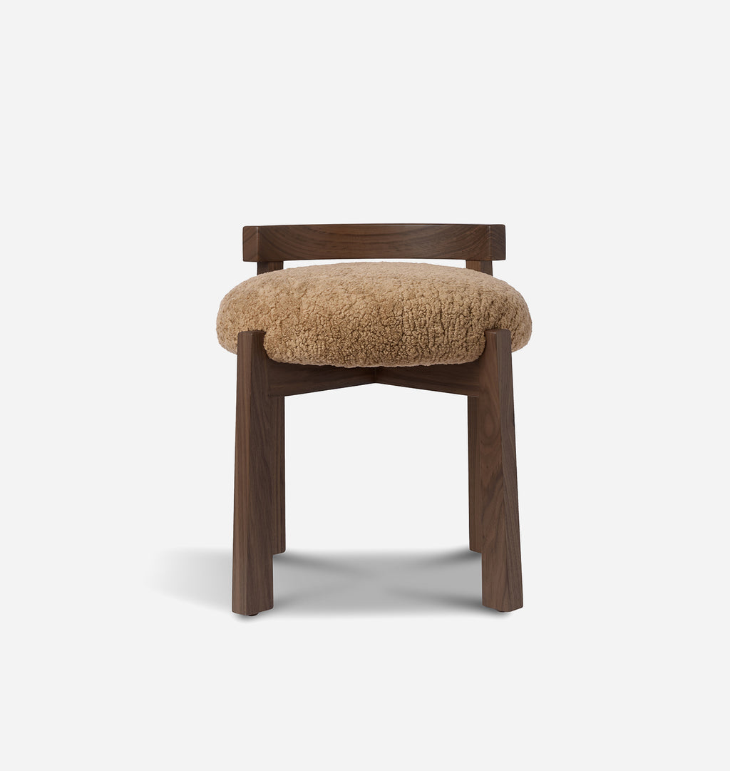 A modern wooden stool with a dark brown frame and a round, fluffy tan shearling seat cushion, shown against a plain light gray background.