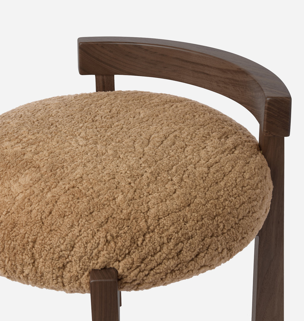 Close-up of a modern chair featuring a round, textured beige shearling seat cushion and a curved dark walnut wood frame against a clean white background.