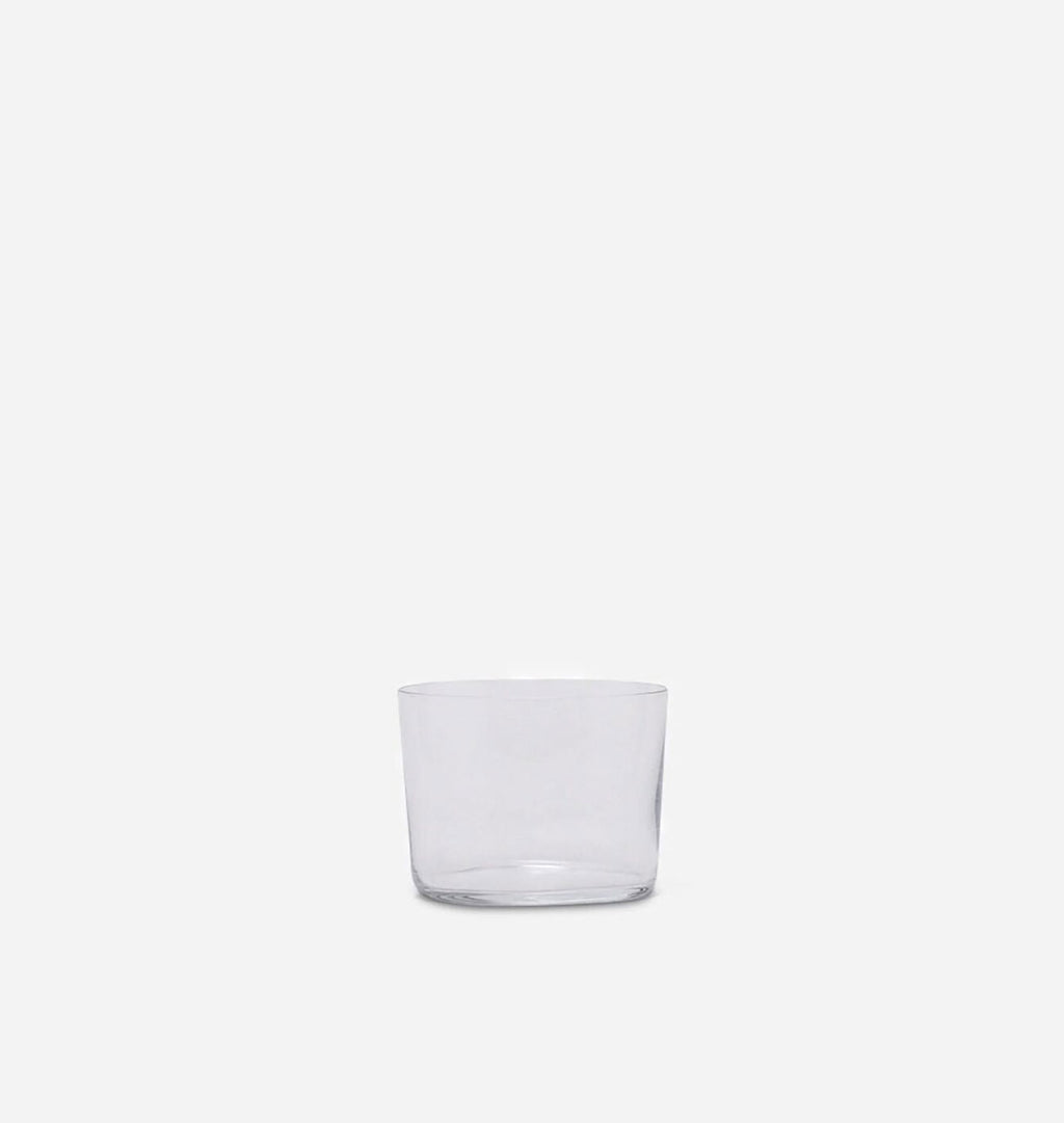 A clear glass tumbler with a thick base, photographed against a solid light gray background.