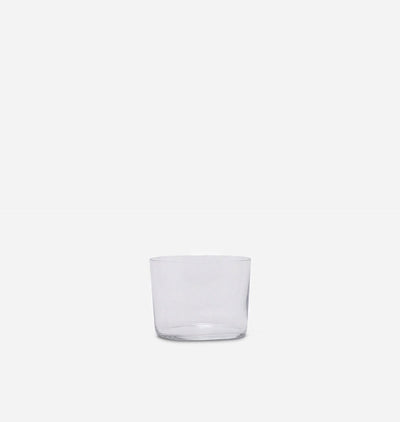 A clear glass tumbler with a thick base, photographed against a solid light gray background.