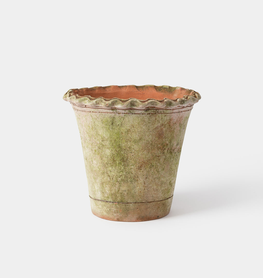 A rustic, hand-painted terracotta planter pot with a scalloped rim, featuring a textured glaze in shades of green and beige with a warm terracotta interior, set against a plain light gray background.