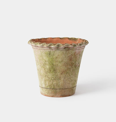 A rustic, hand-painted terracotta planter pot with a scalloped rim, featuring a textured glaze in shades of green and beige with a warm terracotta interior, set against a plain light gray background.