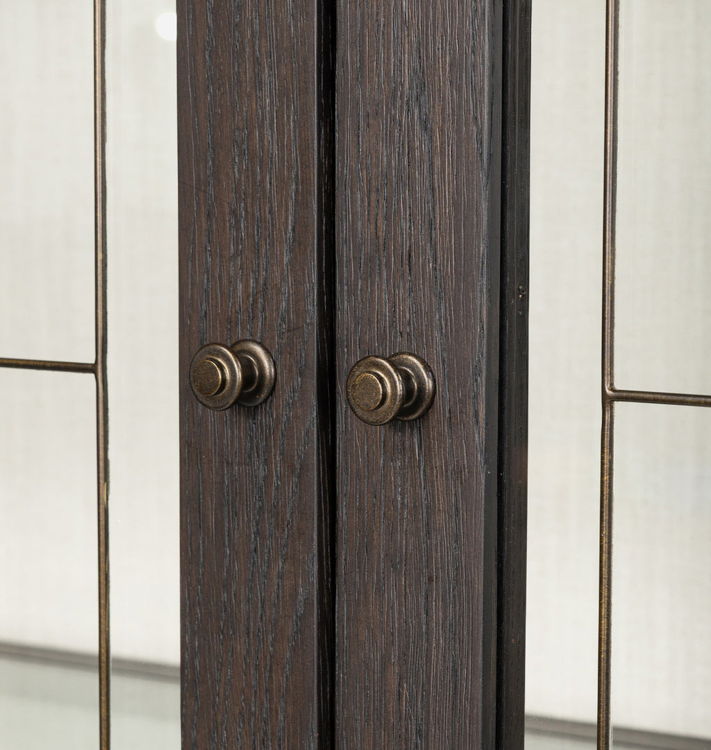 Close-up of dark brown wood cabinet doors with round bronze metal knobs, set against a light beige paneled background.