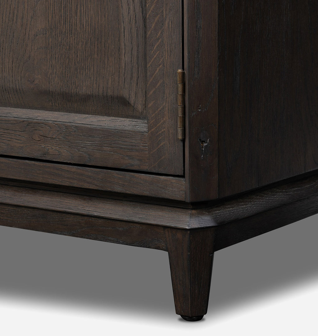 Close-up of a dark brown wooden cabinet corner showing the door, brass hinge, drawer front, leg, and base against a gray studio background.