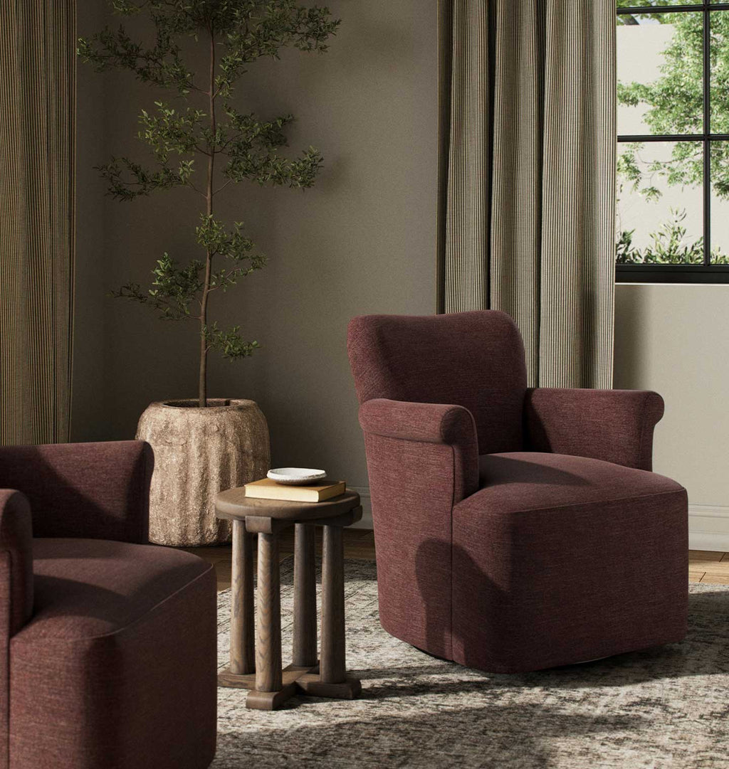 A plush upholstered armchair in deep plum fabric, styled in a modern living room setting with a matching side table and another partial chair.