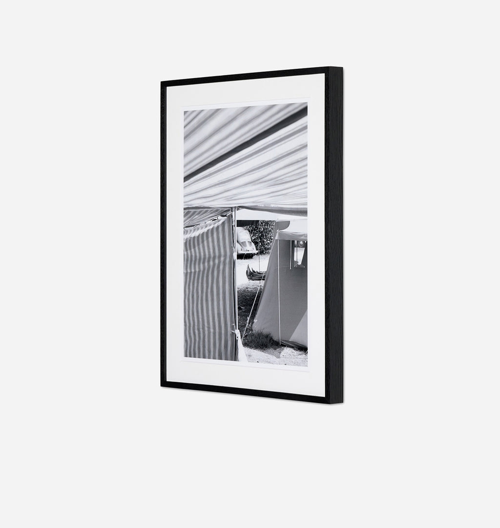 A framed black and white architectural photograph featuring a striped awning and a modern building facade, presented in a black frame with a white mat against a light gray background.