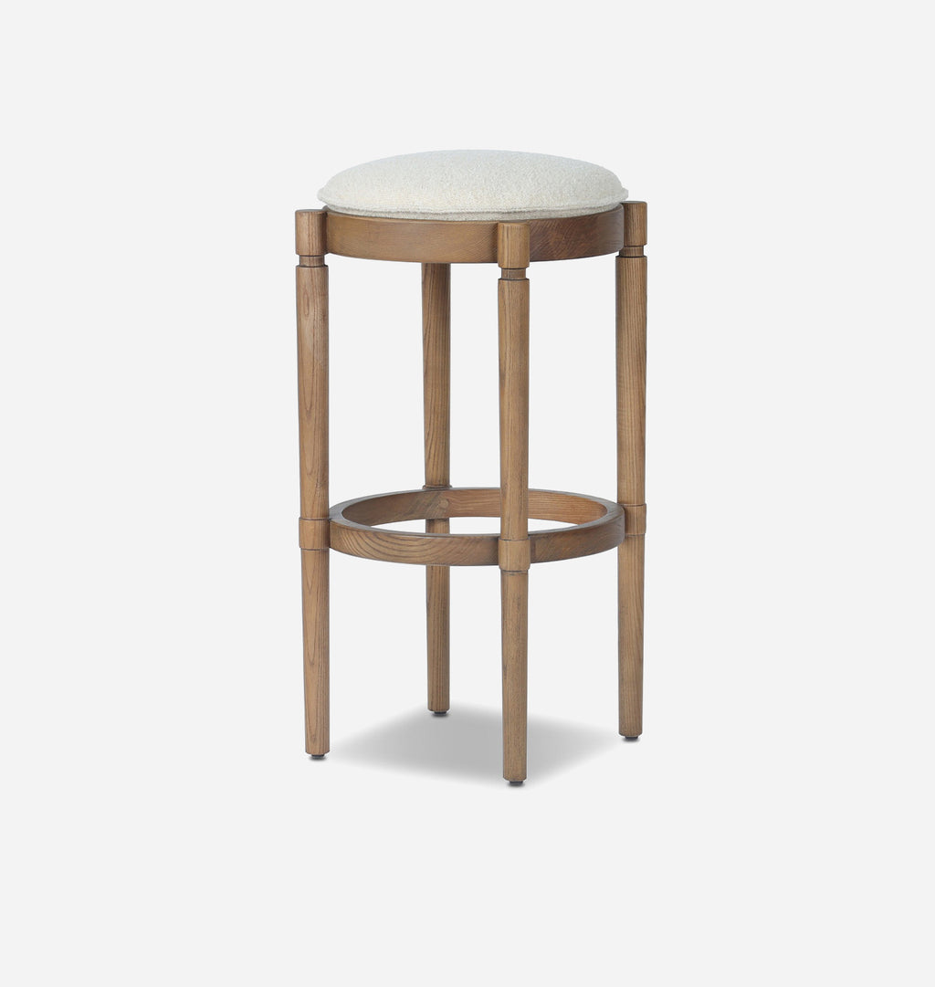 A modern bar stool with a round upholstered seat cushion in a light beige fabric, supported by a light brown wooden frame with a circular footrest.