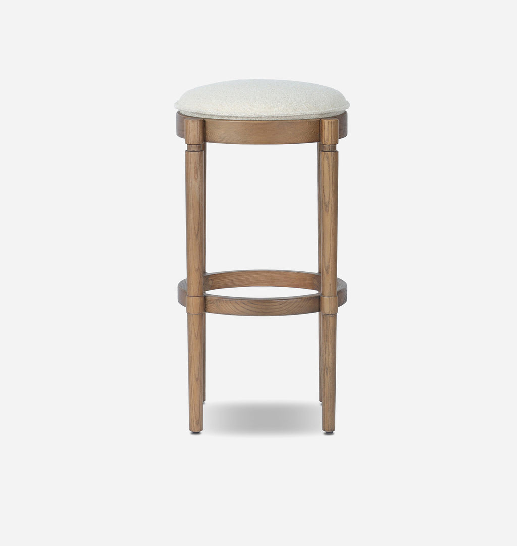 A wooden bar stool with a round upholstered seat cushion in a light cream color, set against a plain light gray background.