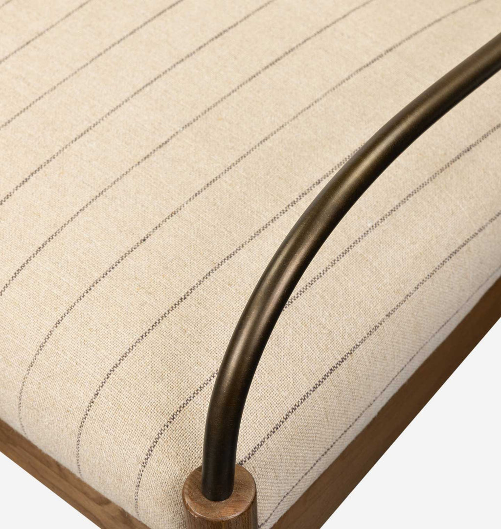 Close-up of a cushioned upholstered furniture corner with a cream fabric seat featuring thin dark pinstripes, a curved dark metal armrest, and a light wood frame.