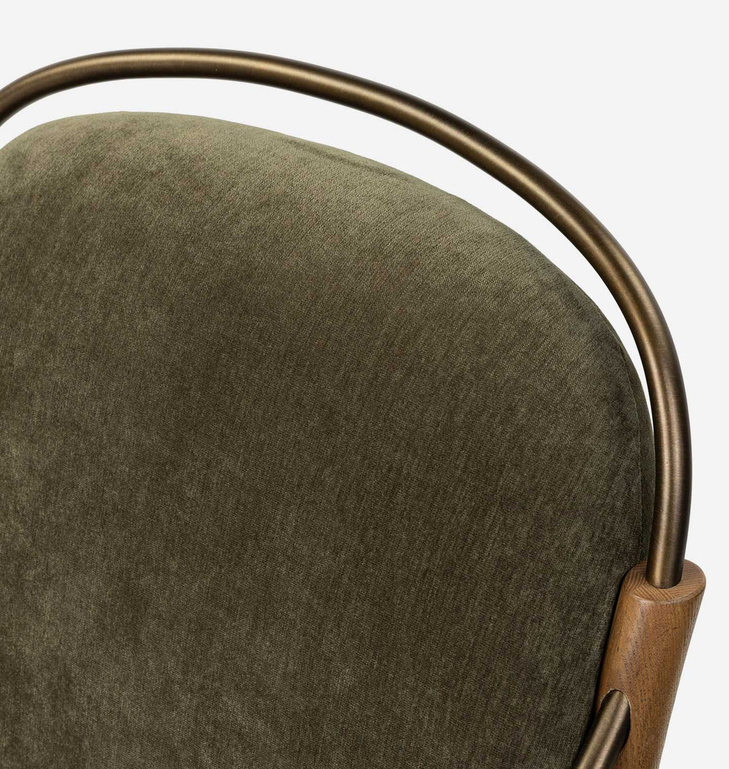 Close-up of a chair cushion in textured olive green fabric, framed by a curved bronze metal support and a small section of natural wood.