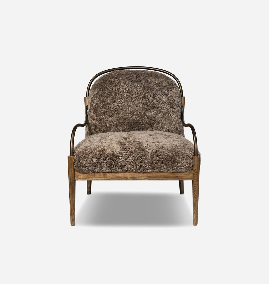 A modern accent chair featuring textured brown sheepskin upholstery on the seat and curved backrest, supported by a natural wood frame with a curved black metal armrest.